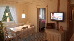 Um quarto aconchegante com mesa de jantar, cadeiras, televisão na parede e janela com cortinas.
