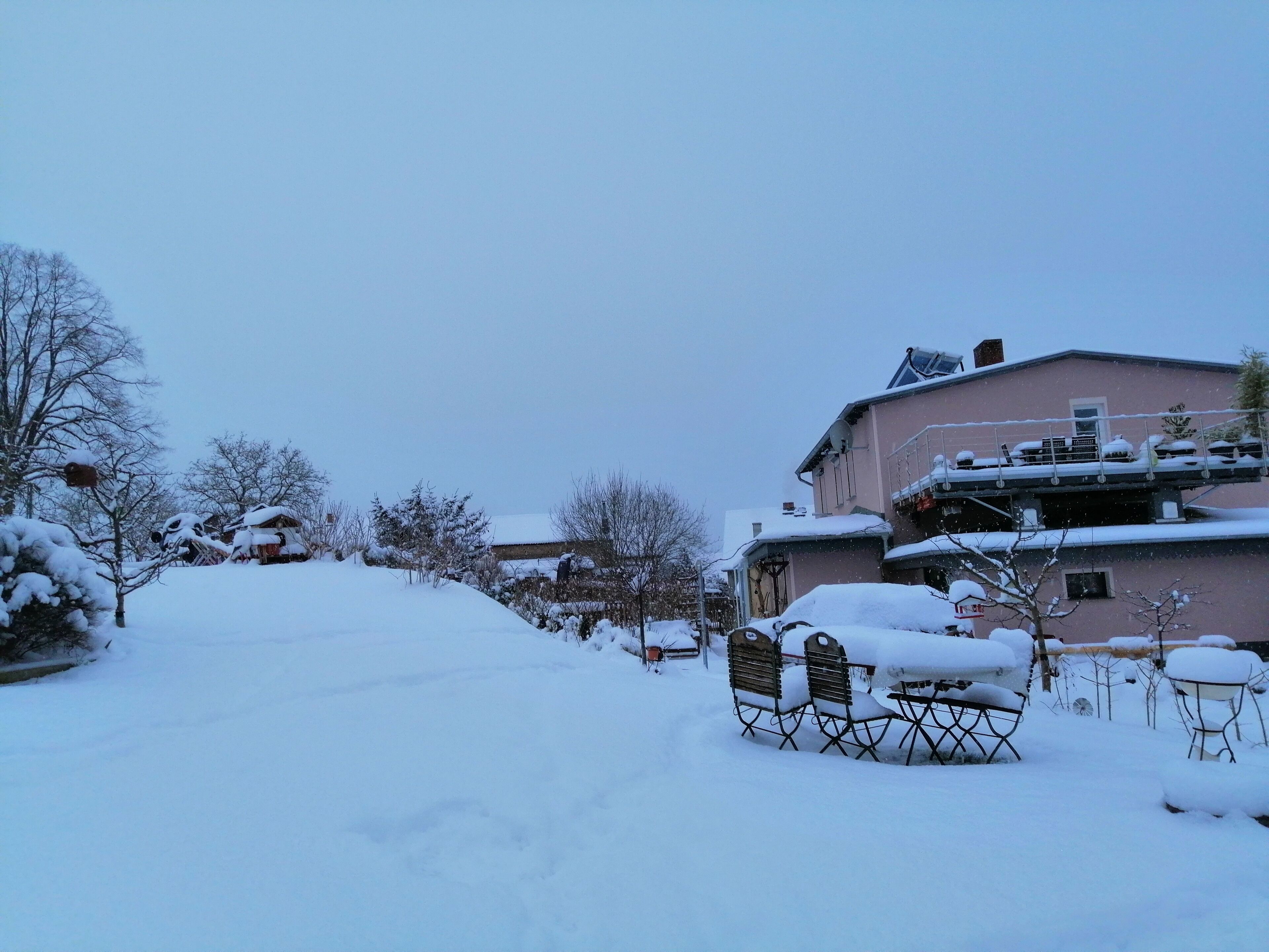 Ein verschneiter Wohnbereich mit Häusern und einer Terrasse mit Gartenmöbeln.