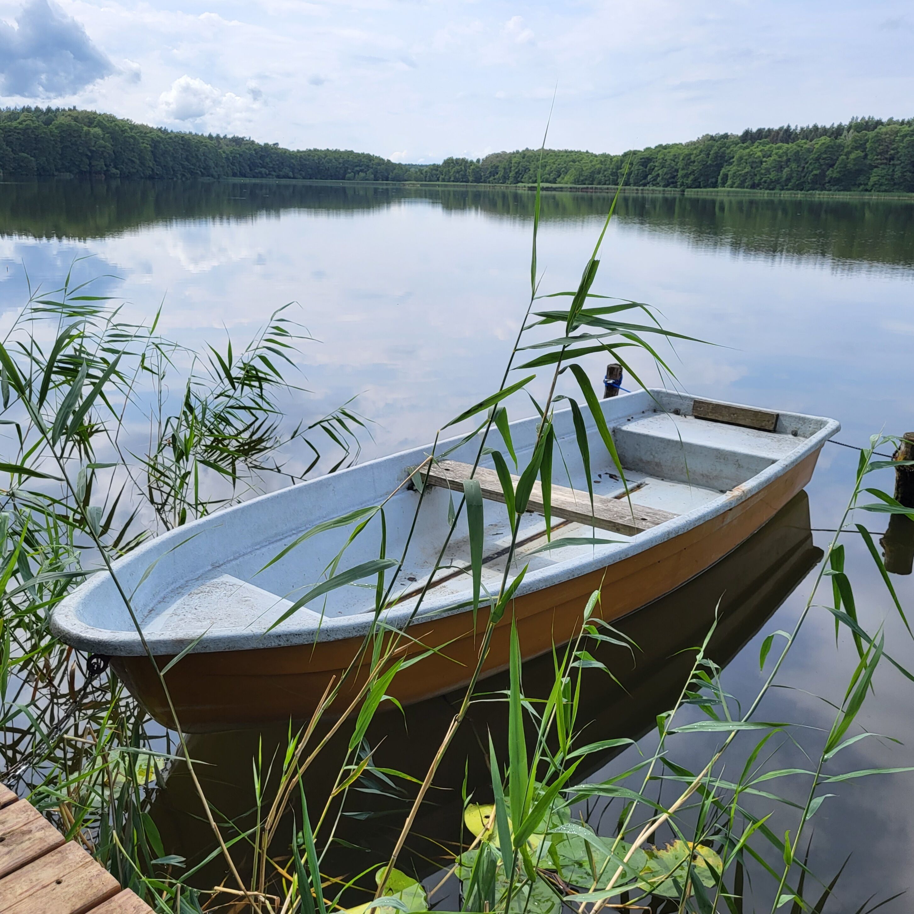 A small wooden boat docked at a wooden pier with a calm lake and forested hills in the background.
