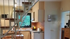 Un vaste espace de vie comprenant un escalier menant à une cuisine, un coin repas et un espace détente agrémenté d’un tapis.