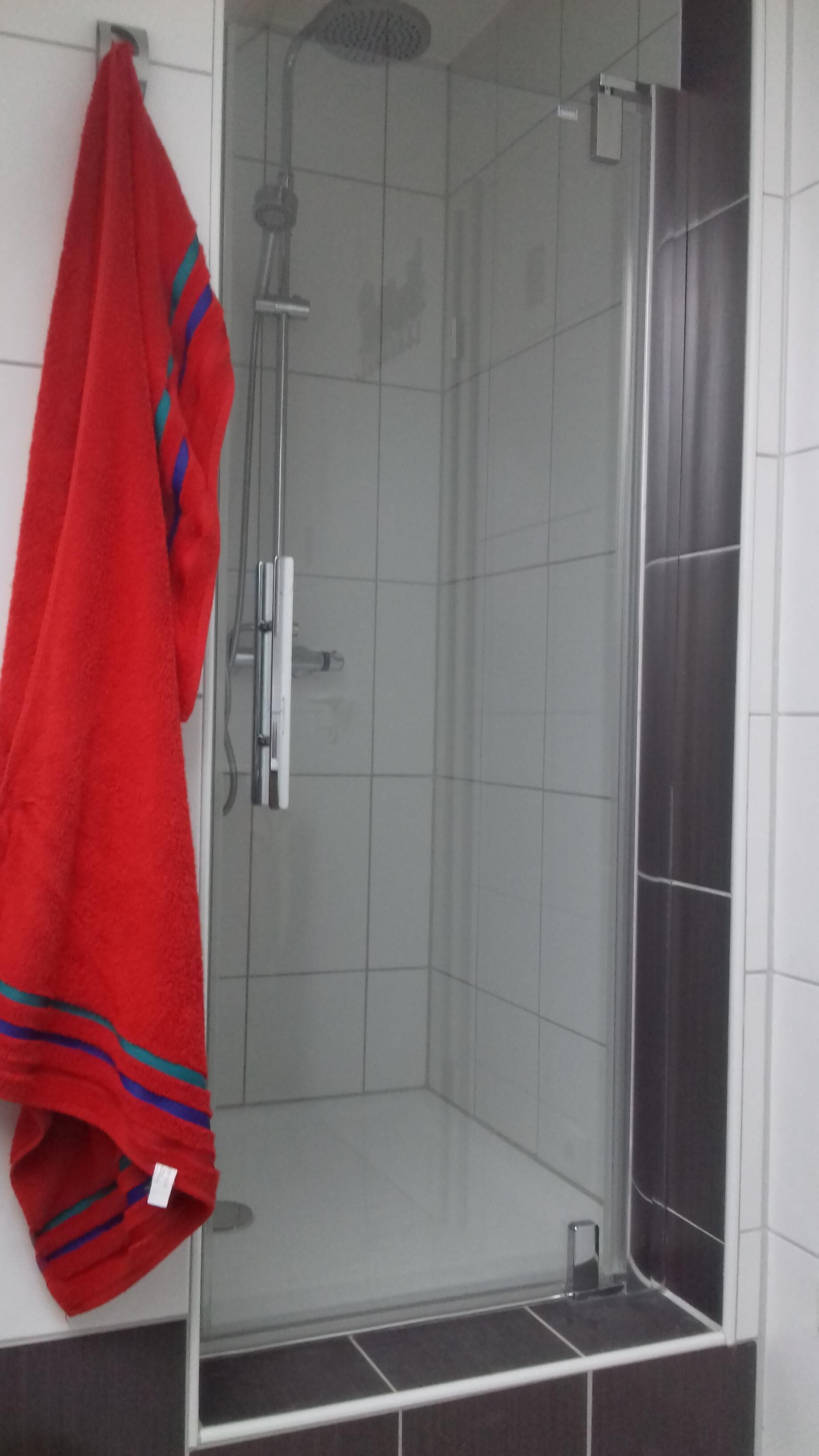 Un espace douche doté d’une porte en verre, une serviette rouge accrochée au mur et des murs recouverts de carreaux.