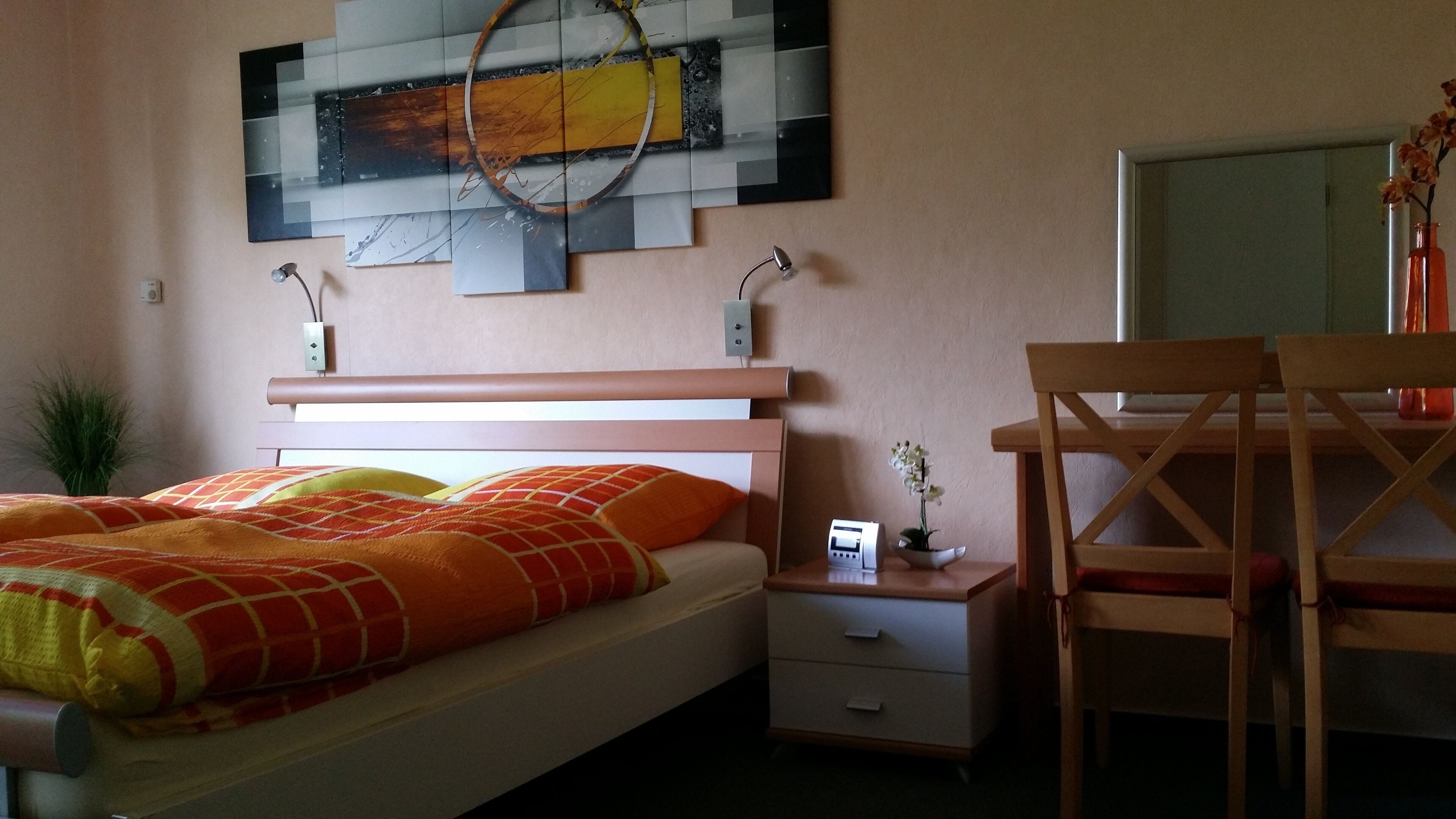 Ein Schlafzimmer mit Bett, Nachttisch, Lampe und Schreibtisch mit Stühlen.