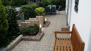 Une terrasse dallée avec un banc en bois, des jardinières en pierre et du mobilier d’extérieur.