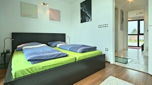 A modern bedroom with a large bed, a nightstand, and a desk lamp. There are framed pictures on the wall and a view of the outdoors through a glass door. - PREMIUM VACATION HOME WITH SEAVIEW (Funtana)
