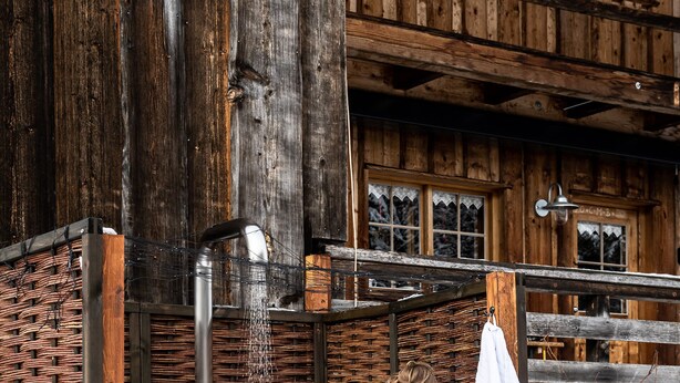 Eine Person in einem weißen Bademantel steht in einer Holzkonstruktion mit einer Dusche.