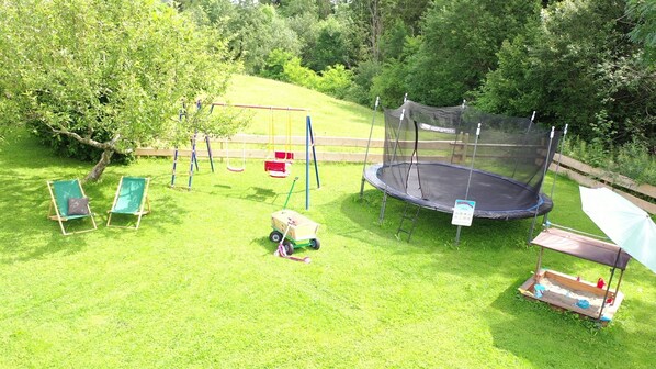 A grassy outdoor area with a trampoline, swings, and a sandbox. - Landsitz Rocky Docky – Holiday Home with Sauna, Garden & Sleeping Pod (Waltenhofen)
