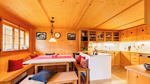Ein Holzblockhaus-Interieur mit Essbereich, Küche und einer Sitzbank mit Kissen.