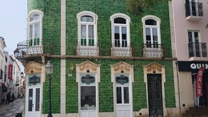 Un bâtiment historique à la façade recouverte de carreaux verts, doté de nombreuses fenêtres et donnant sur une place pavée.