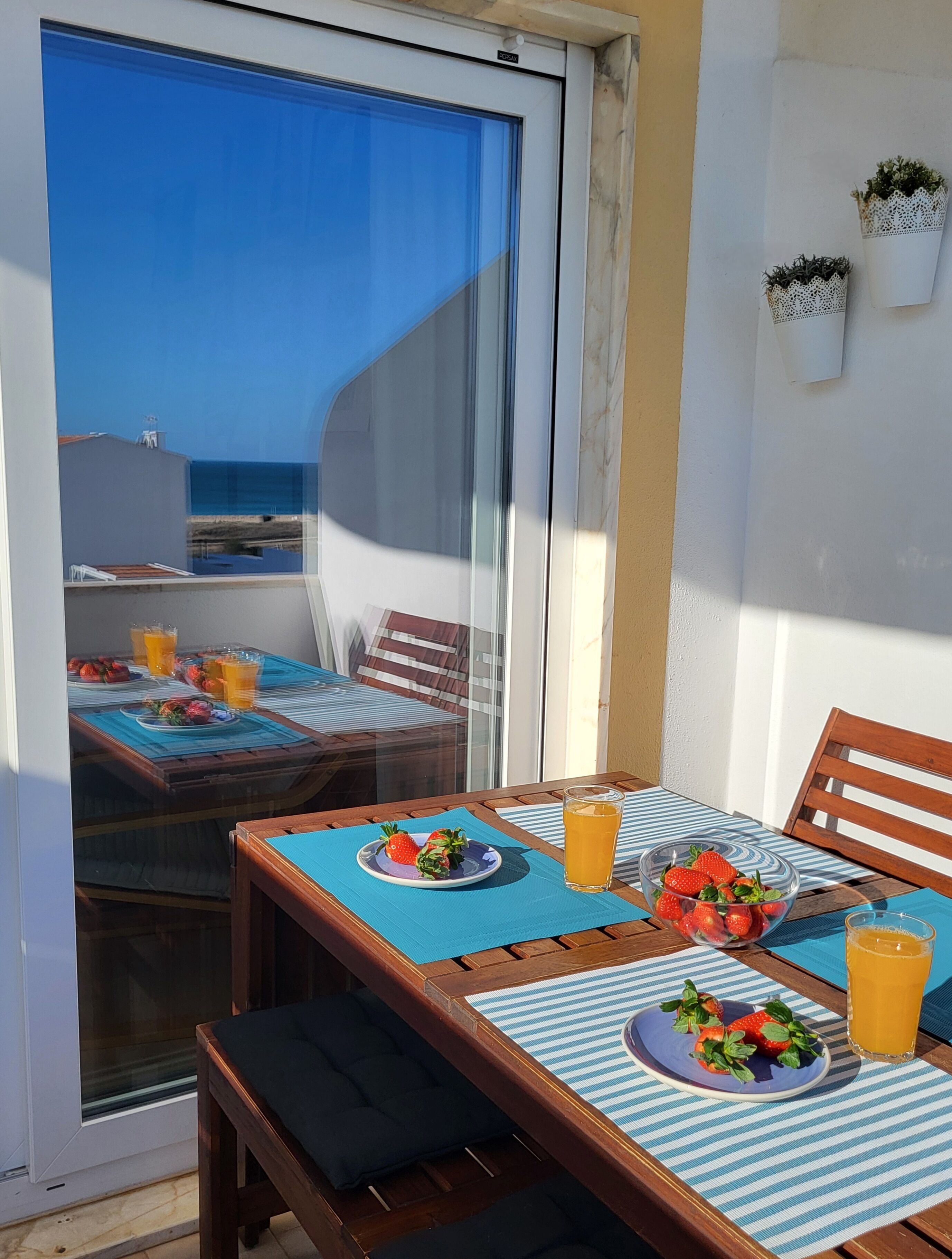 A balcony with a table set for breakfast, including plates of strawberries and glasses of orange juice.