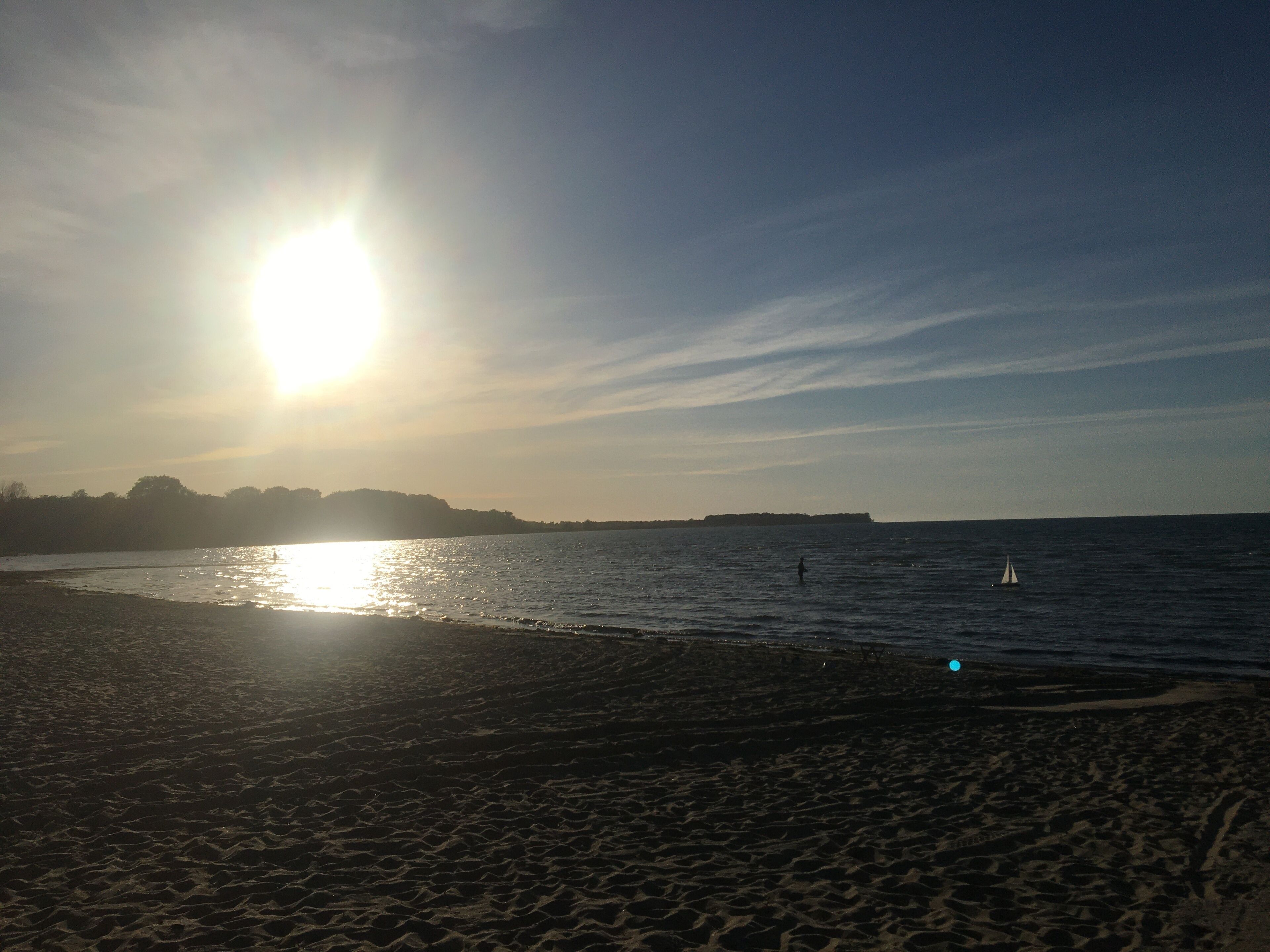 Una playa con cielo despejado, el sol reflejado en el agua y una masa de tierra a lo lejos.