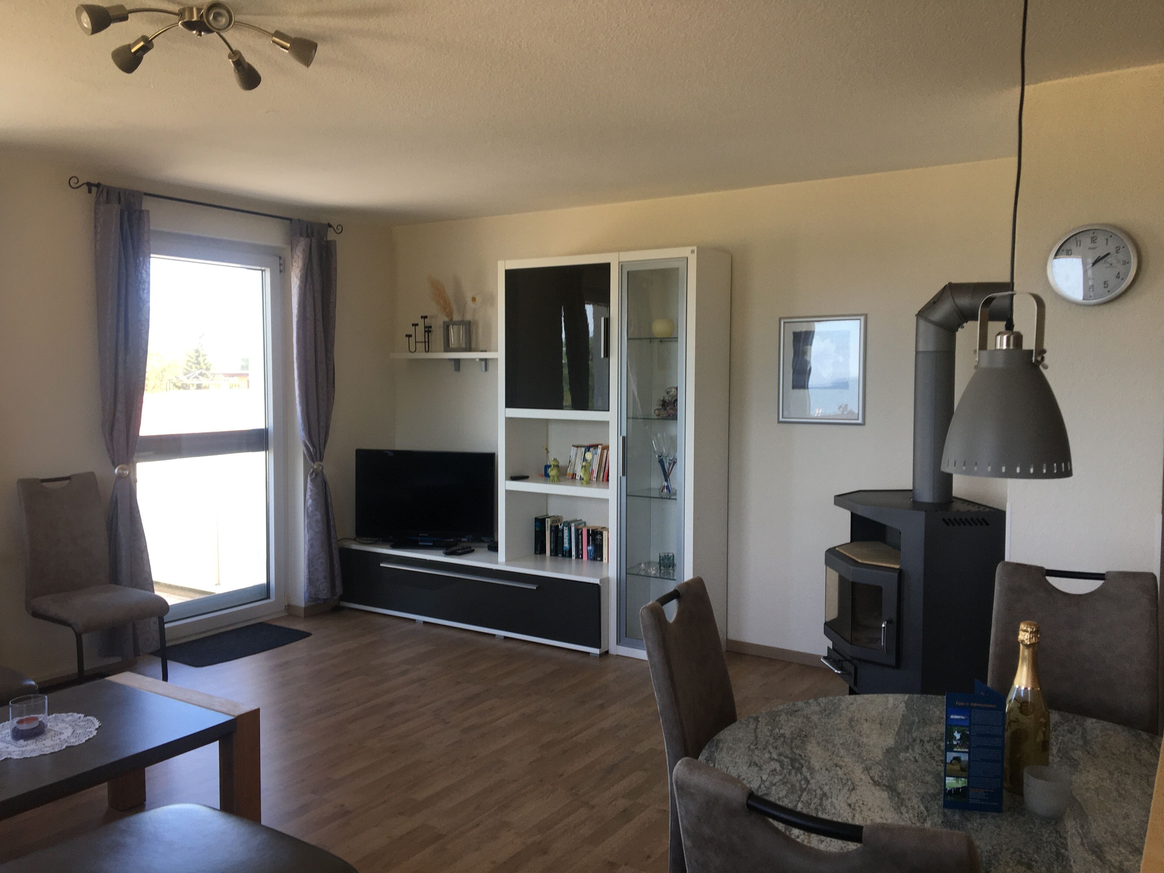 A modern living room with a flat-screen TV, a fireplace, a dining area, and a large window with curtains.