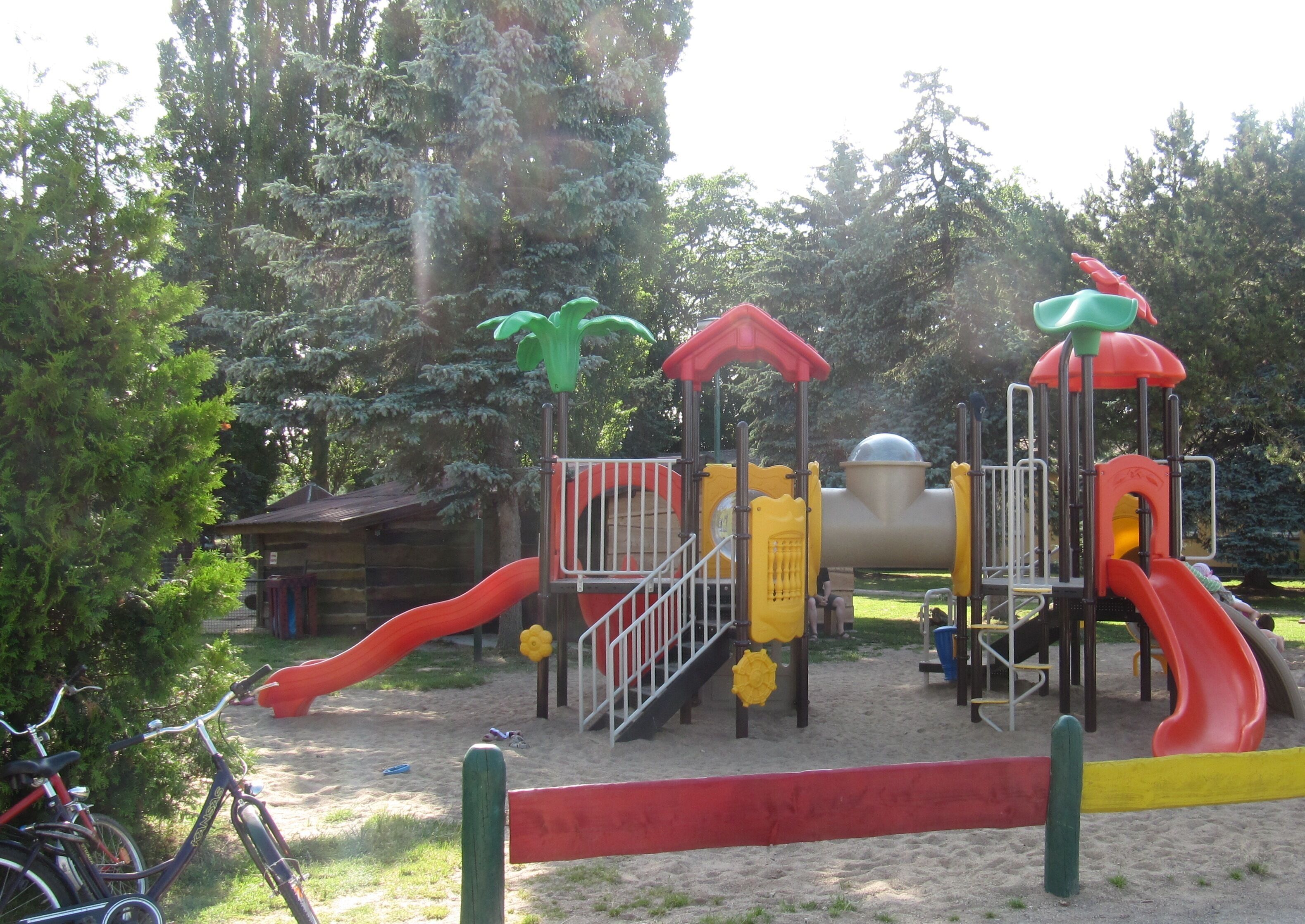 Ein Spielplatz mit Rutschen und Klettergerüsten, umgeben von Bäumen und einem Sandbereich.