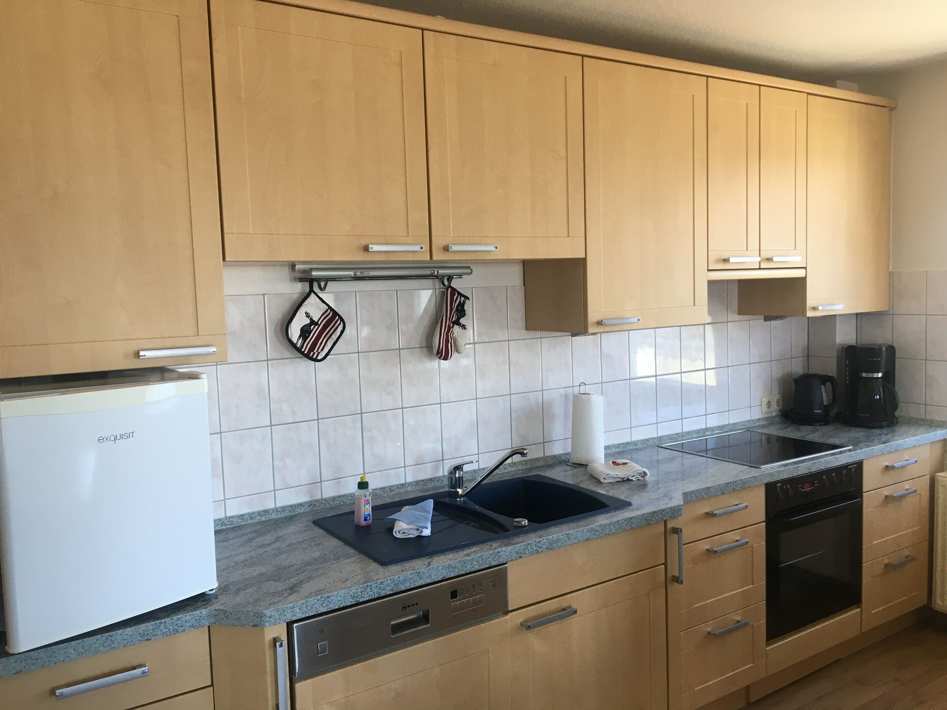 Een keuken met lichte houten kastjes, een witte koelkast, een wastafel met een handdoek en een koffiezetapparaat.