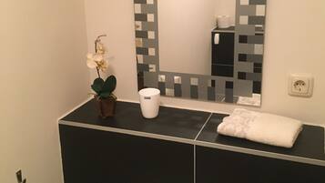 Ein Badezimmer mit schwarz-weiß gefliesten Wänden, einem weißen Waschbecken, einem Spiegel mit schwarz-weißem Muster, einer Topfpflanze, einer weißen Tasse und einer Handseifenflasche.