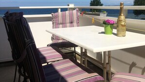 A terrace with a white table and striped chairs, a bottle of champagne, and a view of the sea. - Baltic Sea view from all windows, 50m to the beach (Zierow)