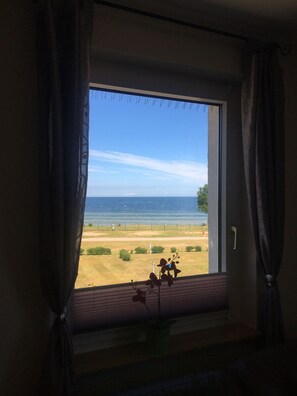 Une pièce dotée d’une grande fenêtre donnant sur une plage et la mer.