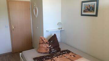 A bedroom with a bed, pillows, a door, a wall-mounted shelf, and a framed picture.