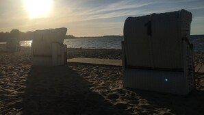 A beach with two white beach chairs facing the sea, a wooden walkway leading to the water, and the sun setting in the background. - Baltic Sea view from all windows, 50m to the beach (Zierow)