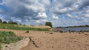 Une plage de sable avec des empreintes de pas, un sentier pavé de pierres et une étendue d'eau en arrière-plan.