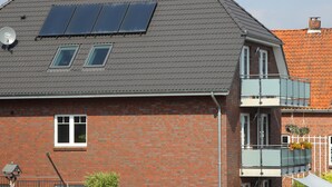 Une maison à deux étages, dotée d’un toit en pente, de panneaux solaires, d’un balcon orné de jardinières suspendues et d’une antenne parabolique.