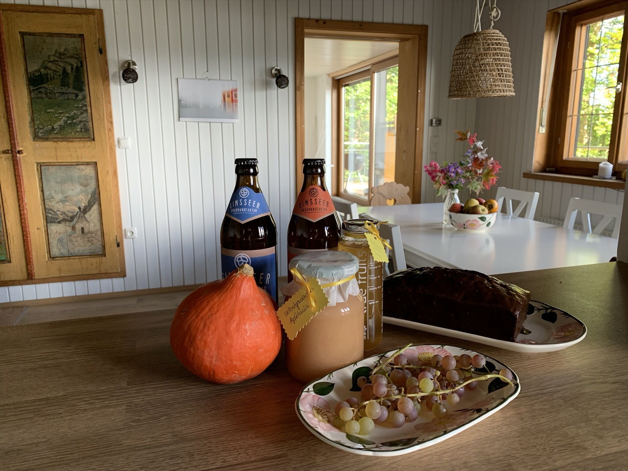 A wooden table with a pumpkin, bottles, a jar, and a plate of grapes.