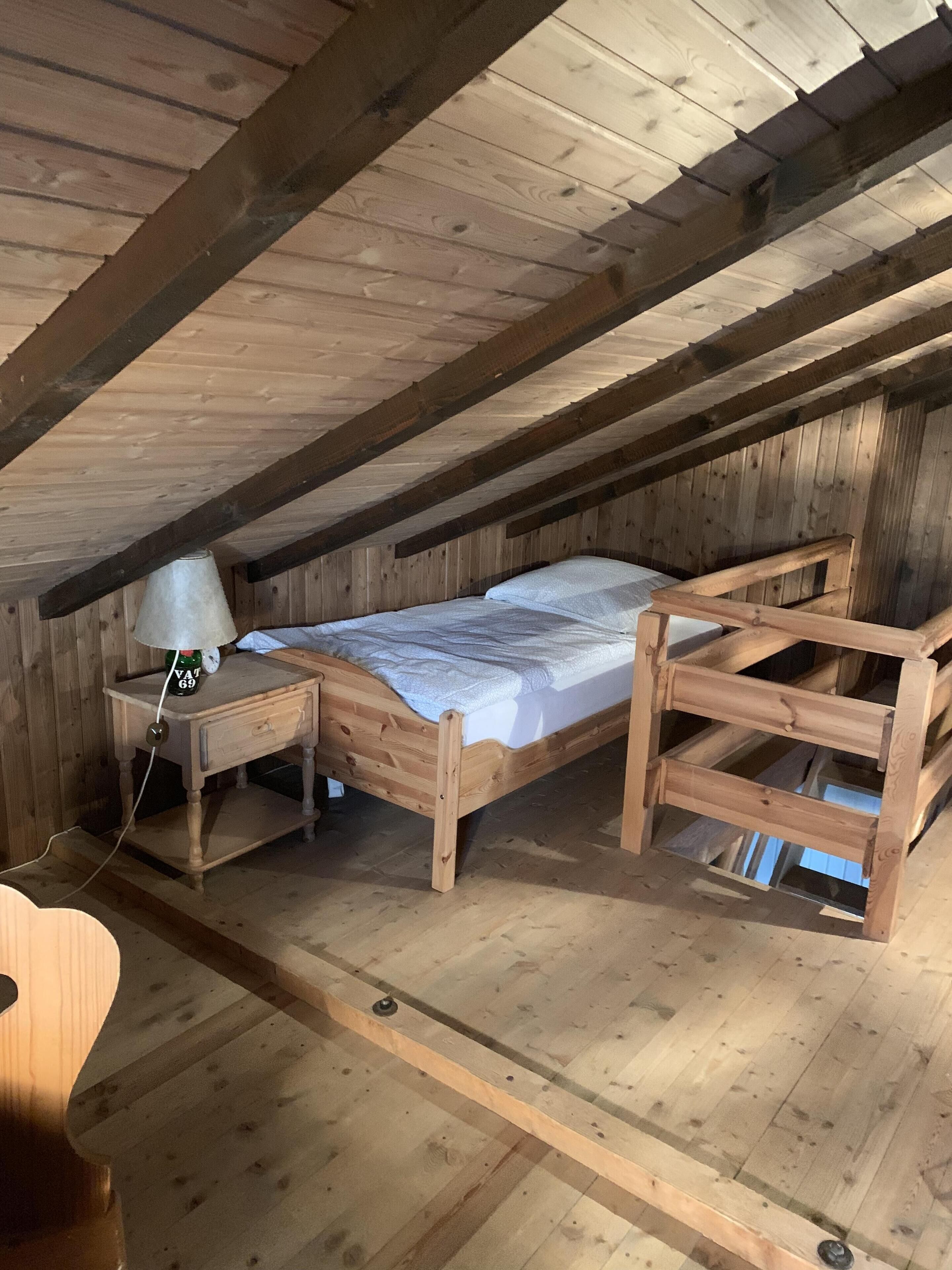 A wooden loft bedroom with a single bed, a nightstand, and a lamp.