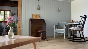 Um quarto aconchegante com uma mesa de madeira, uma cadeira de vime, uma cadeira de balanço e um baú de gavetas antigo.