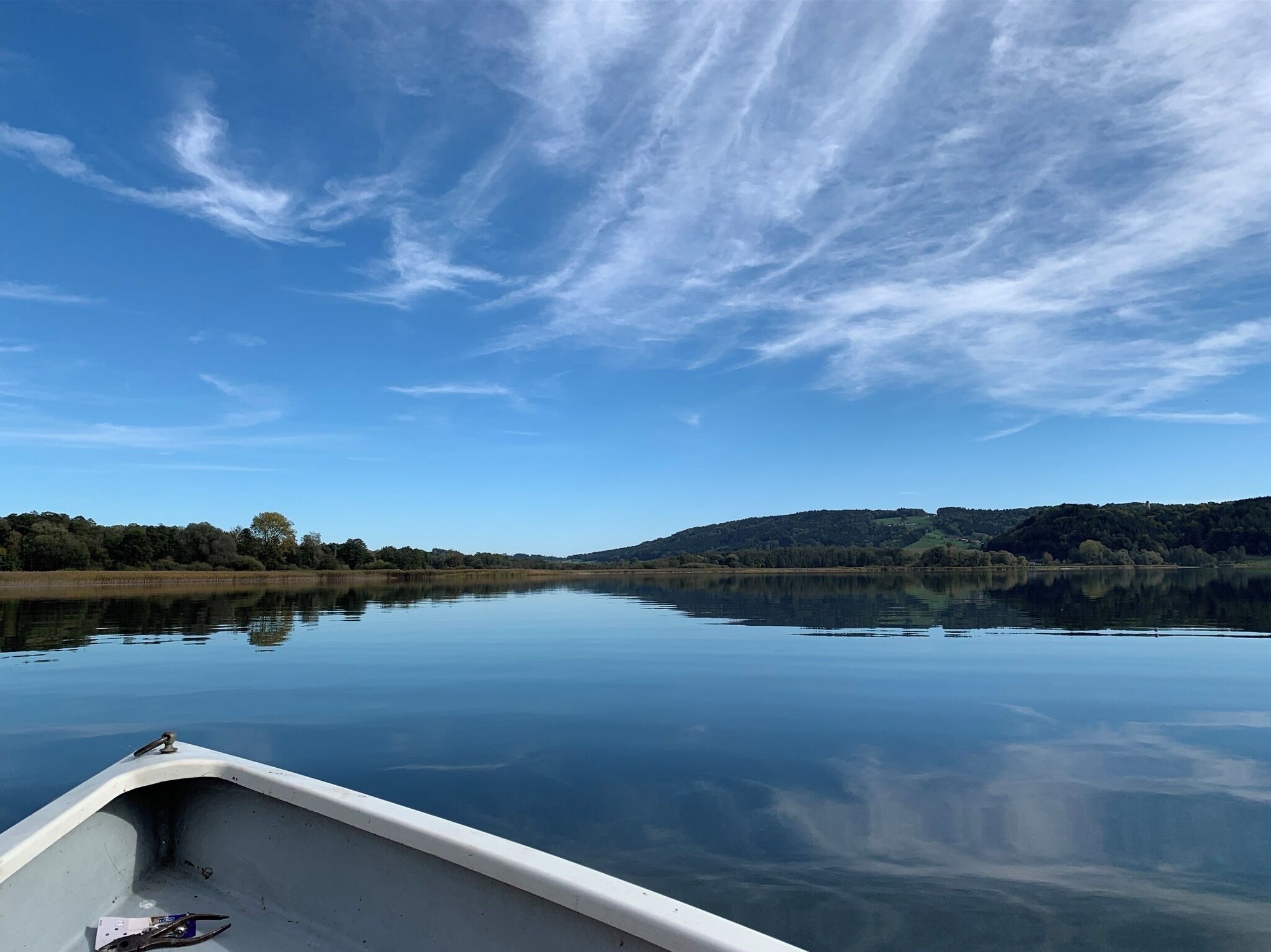Un lac paisible, avec un bateau au premier plan et une colline boisée à l’arrière-plan, sous un ciel dégagé.