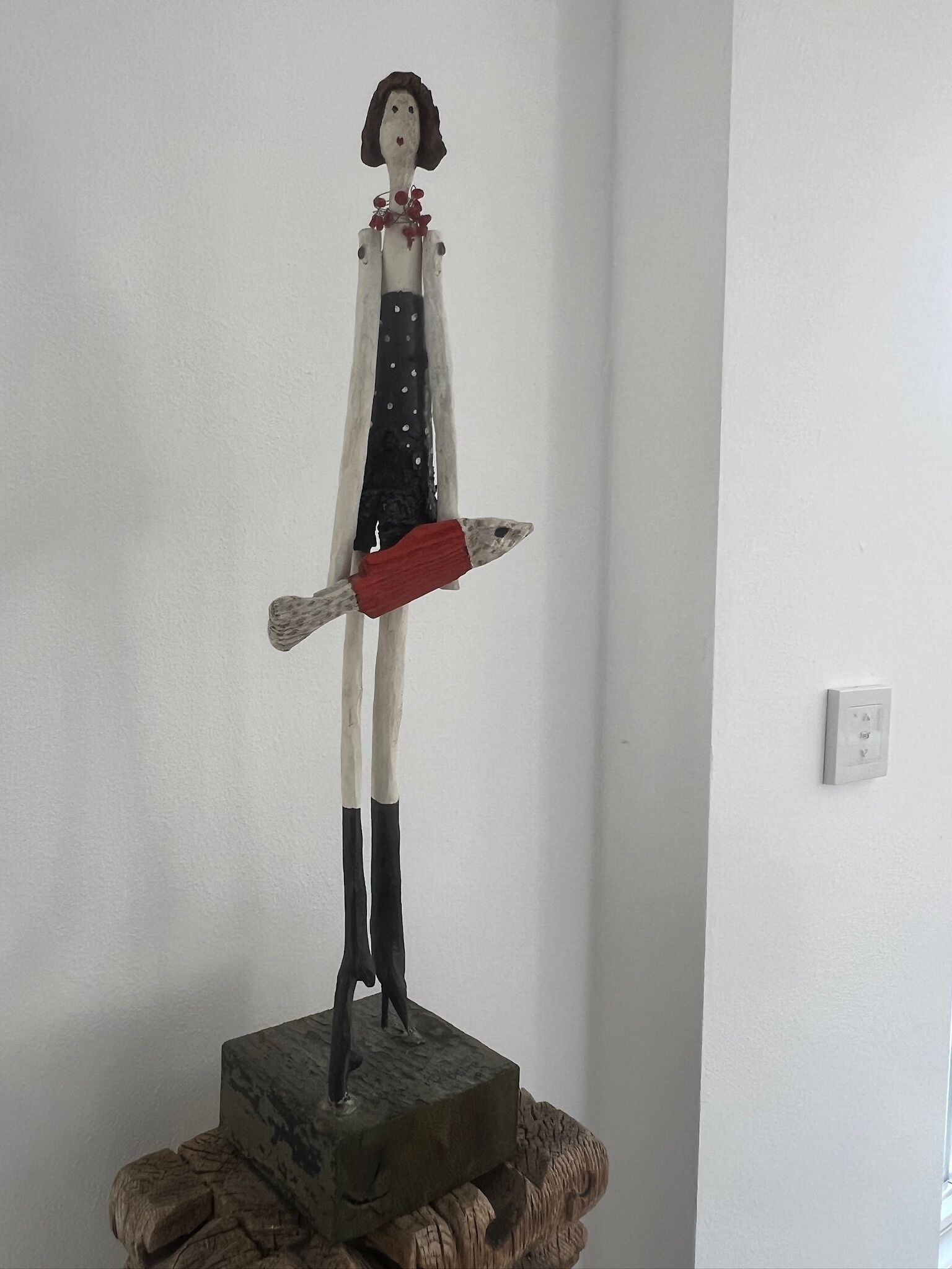 Een sculptuur van een figuur op een houten voetstuk.