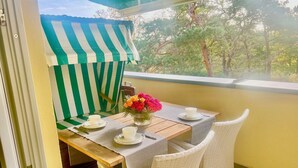 A balcony with a table set for two, a striped awning, and a view of trees. - Comfortable penthouse apartment with 5 stars, 50 m to beach (Mecklenburg Vorpommern)