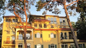 A multi-story building with balconies and arched windows, surrounded by trees and greenery. - Comfortable penthouse apartment with 5 stars, 50 m to beach (Mecklenburg Vorpommern)