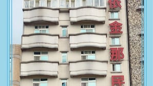 Un hotel de varios pisos con balcones y un local comercial en la planta baja.