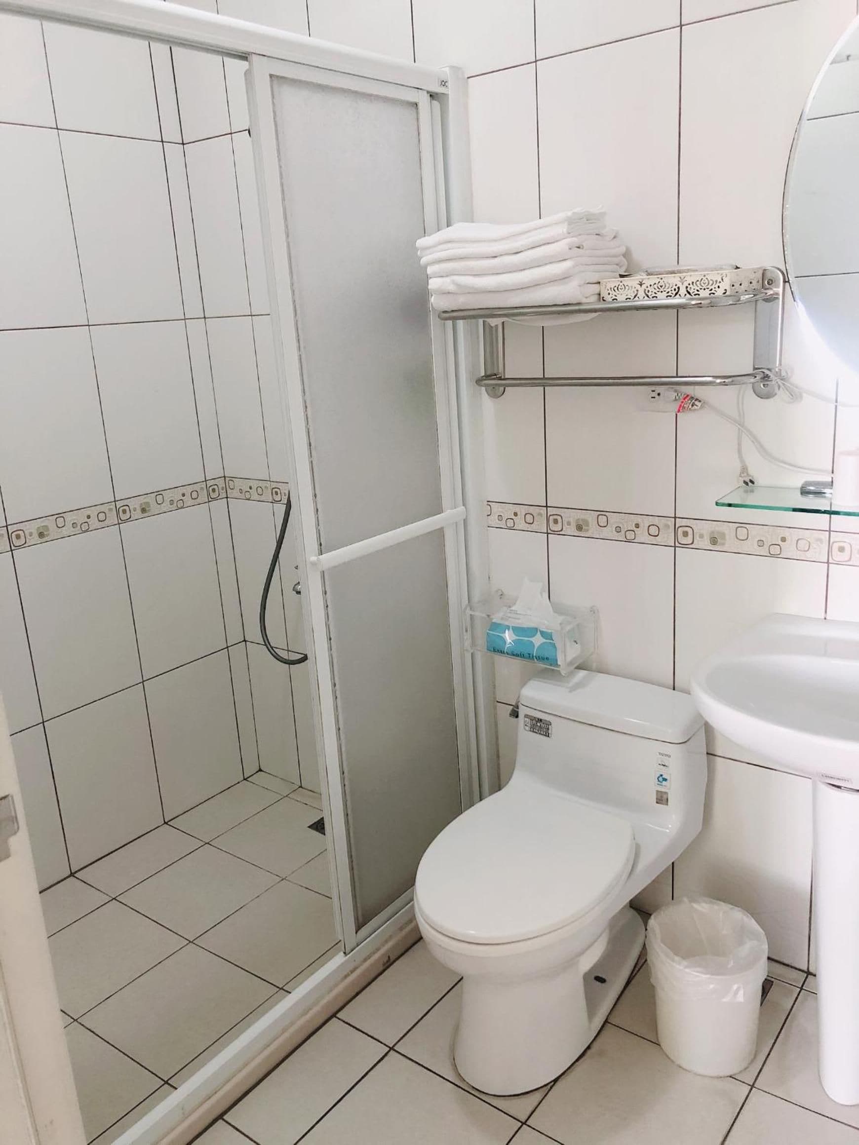A bathroom with a toilet, a glass shower enclosure, a sink, and a towel rack.