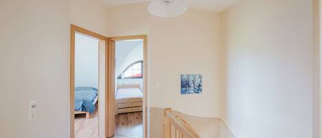 A hallway leading to a bedroom with a wooden floor, a ceiling light, and a painting on the wall.