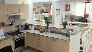 A modern kitchen with granite countertops, a built-in oven, and a sink. There is a dining area with a sofa and a TV. - Vv Apartamento Gran Vista Colony Club (Puerto del Carmen)