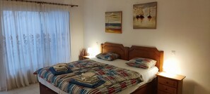 Una cama bien hecha con ropa de cama a rayas y almohadas, una mesita de noche con lámpara, y dos cuadros en la pared.