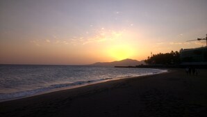 A beach with a sunset, calm sea, and distant mountains. - Vv Apartamento Gran Vista Colony Club (Puerto del Carmen)