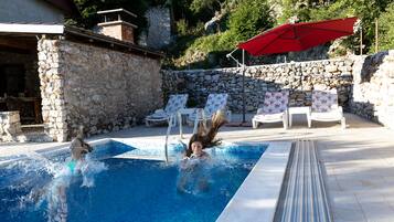 Une piscine avec des murs en pierre, des chaises longues et un parasol rouge.
