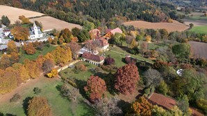 Luchtbeeld van een landelijk gebied met een kerk, een groot huis met rood dak, en omliggende velden.