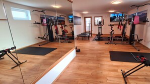 Een sportschool met trainingsapparatuur, houten vloeren en een grote spiegel.
