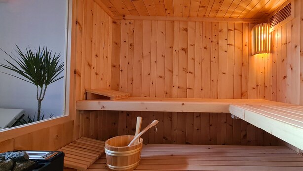 Een houten sauna met banken, een houten emmer en een plant.