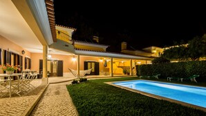 A poolside area with a tiled patio, outdoor seating, and a well-lit building facade. - Modern, large and beautiful villa with pool/garden in Azeitão south of Lisbon. (Azeitão, Setubal)