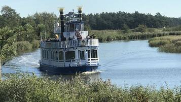 A riverboat with multiple decks and passengers, surrounded by lush greenery.