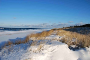 A snowy beach with a clear sky and waves in the background.