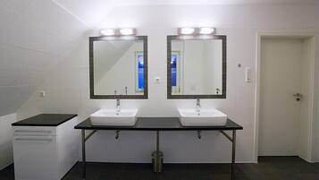 Een openbaar toilet met twee wastafels, een spiegel boven elke wastafel, en een prullenbak in het midden.