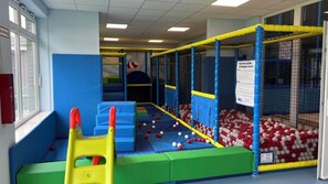 Un espace de jeux intérieur doté de structures de jeu rembourrées, d’une piscine à balles et de filets de sécurité.