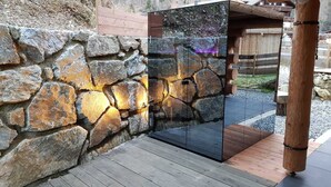 Un muro de piedra con una puerta de cristal, una terraza de madera y una estructura de madera al fondo.
