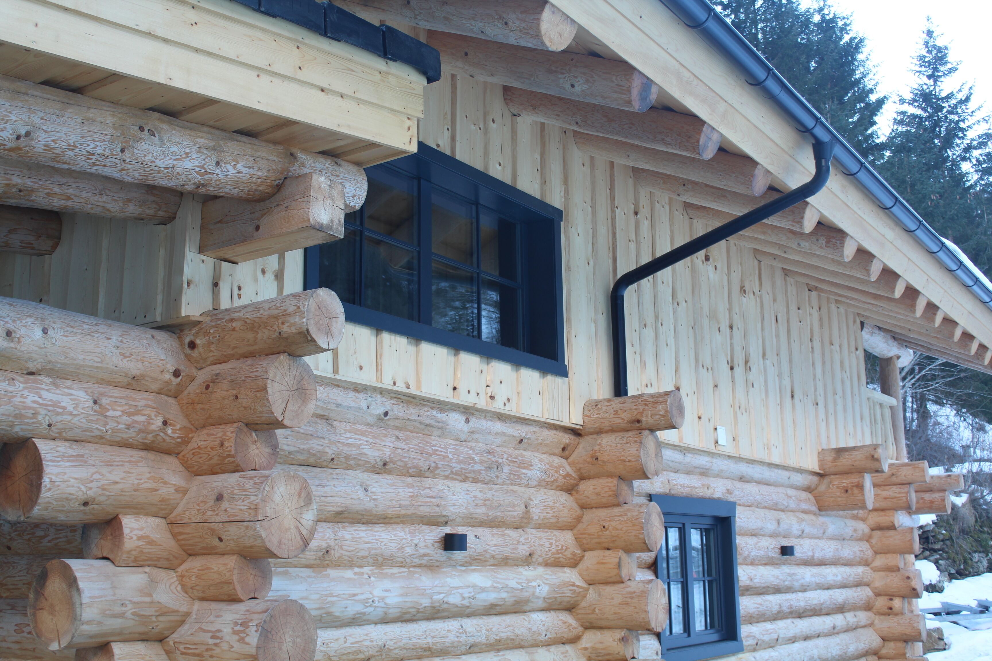 Eine Blockhütte mit Fenster und Tür, mit Holzfassade und Metall-Dachrinne.