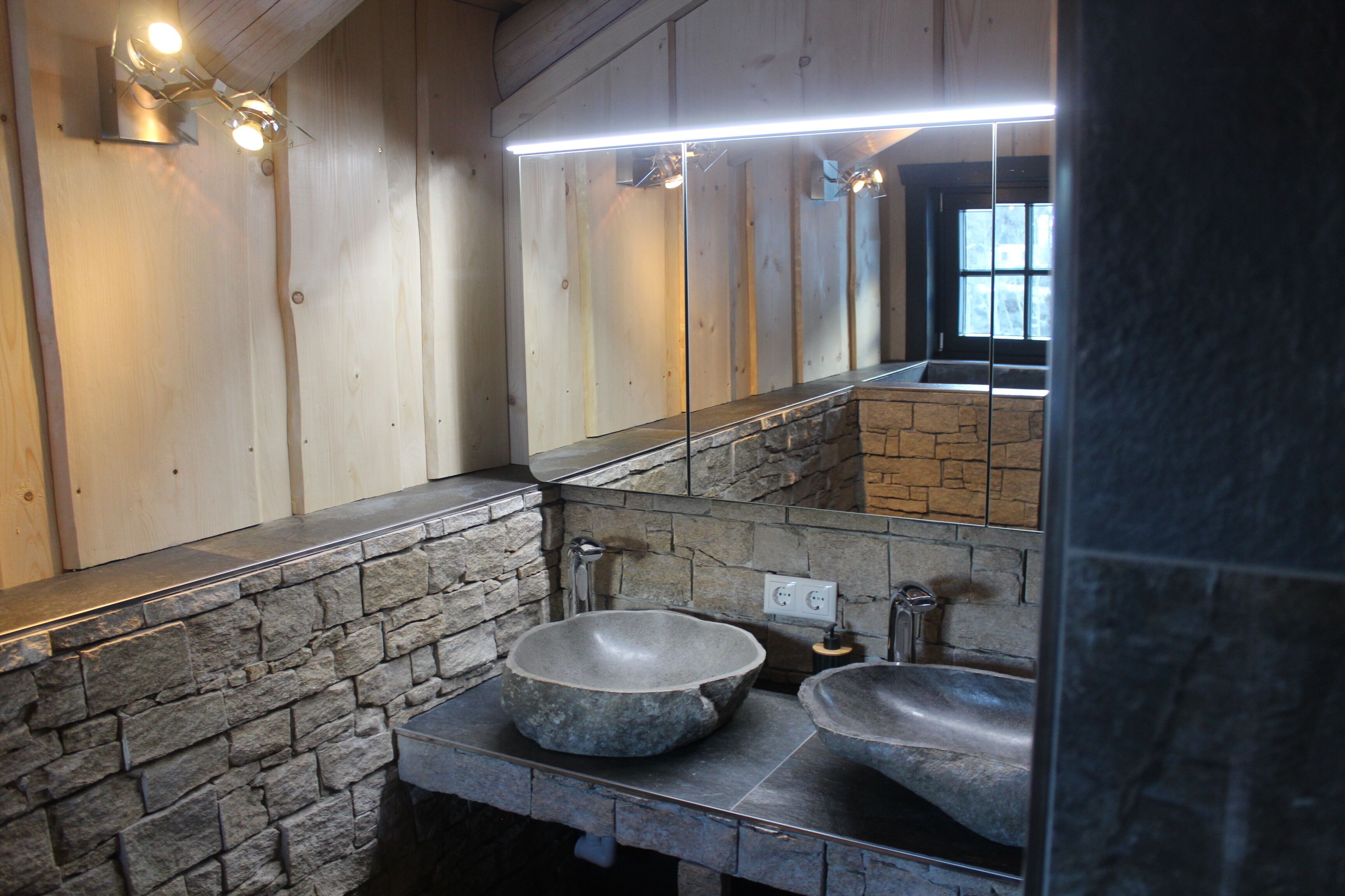 Ein Badezimmer mit einem Waschbecken aus Stein, einem Spiegel und einem beleuchteten Waschtisch.