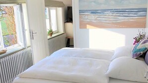 Et soveværelse med en seng, et vindue med udsigt over landskabet, et maleri af stranden og en loftslampe.